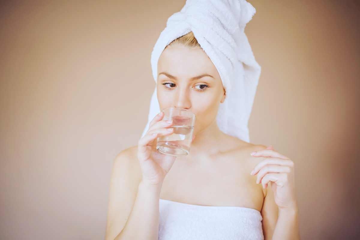 Ragazza con asciugamano e turbante che beve un bicchiere d'acqua 