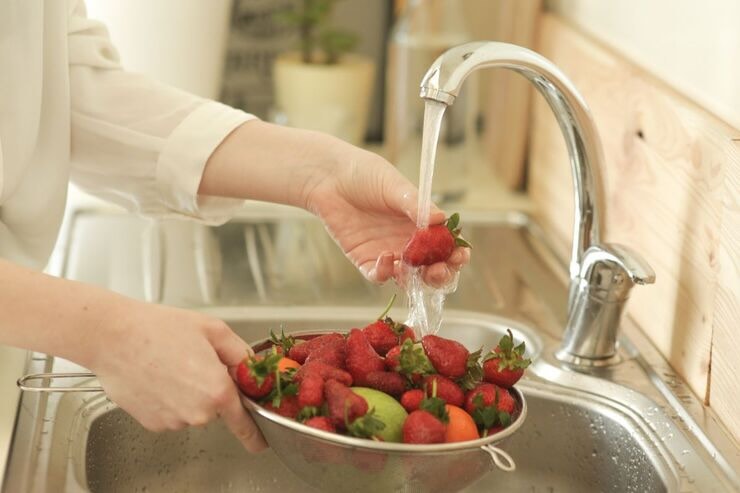 Mani di donne che lavano frutta e fragole sotto il getto dell'acqua del rubinetto 