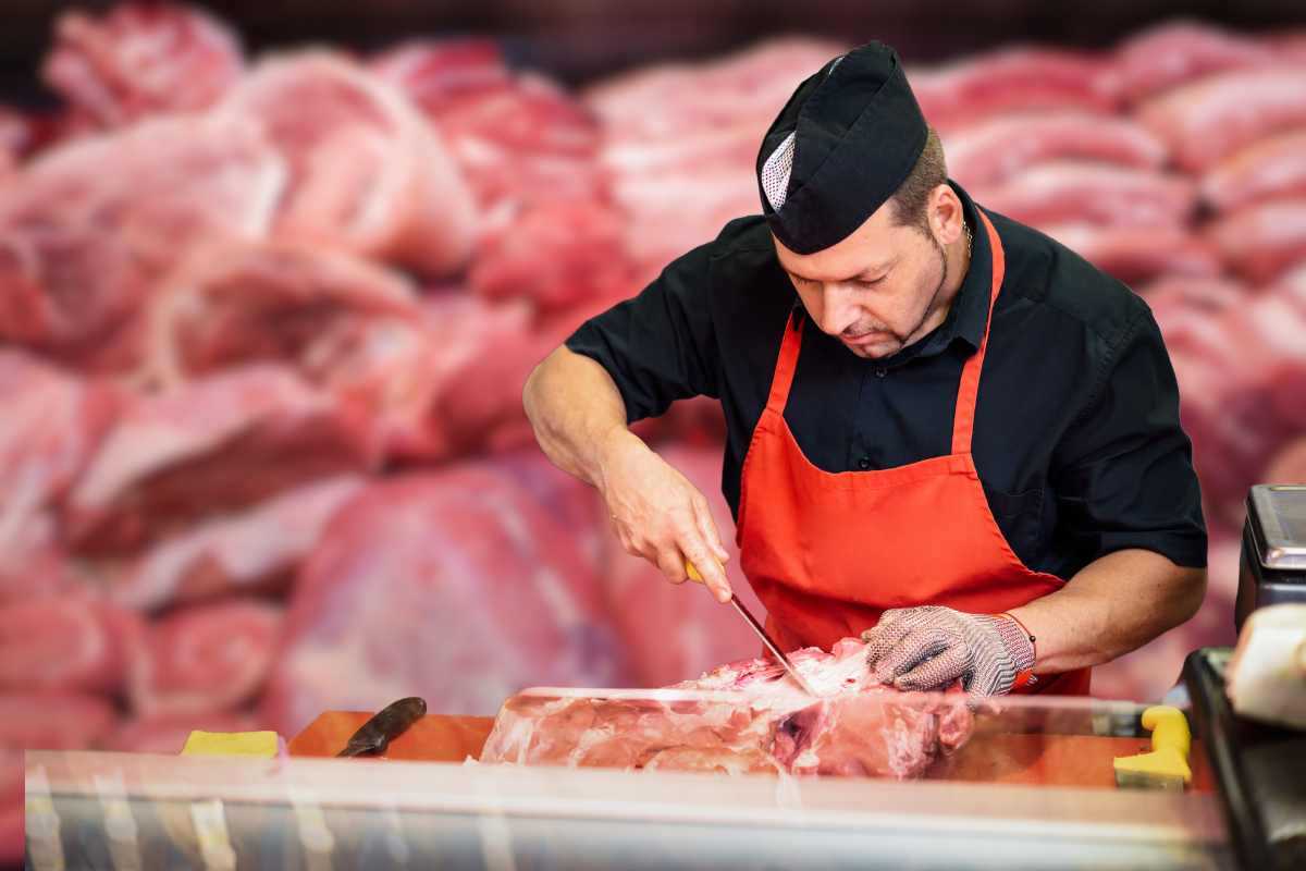 Macellaio che affetta la carne sullo sfondo tanta carne congelata