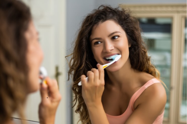 ragazza con capelli ricci che usa spazzolino per lavare denti