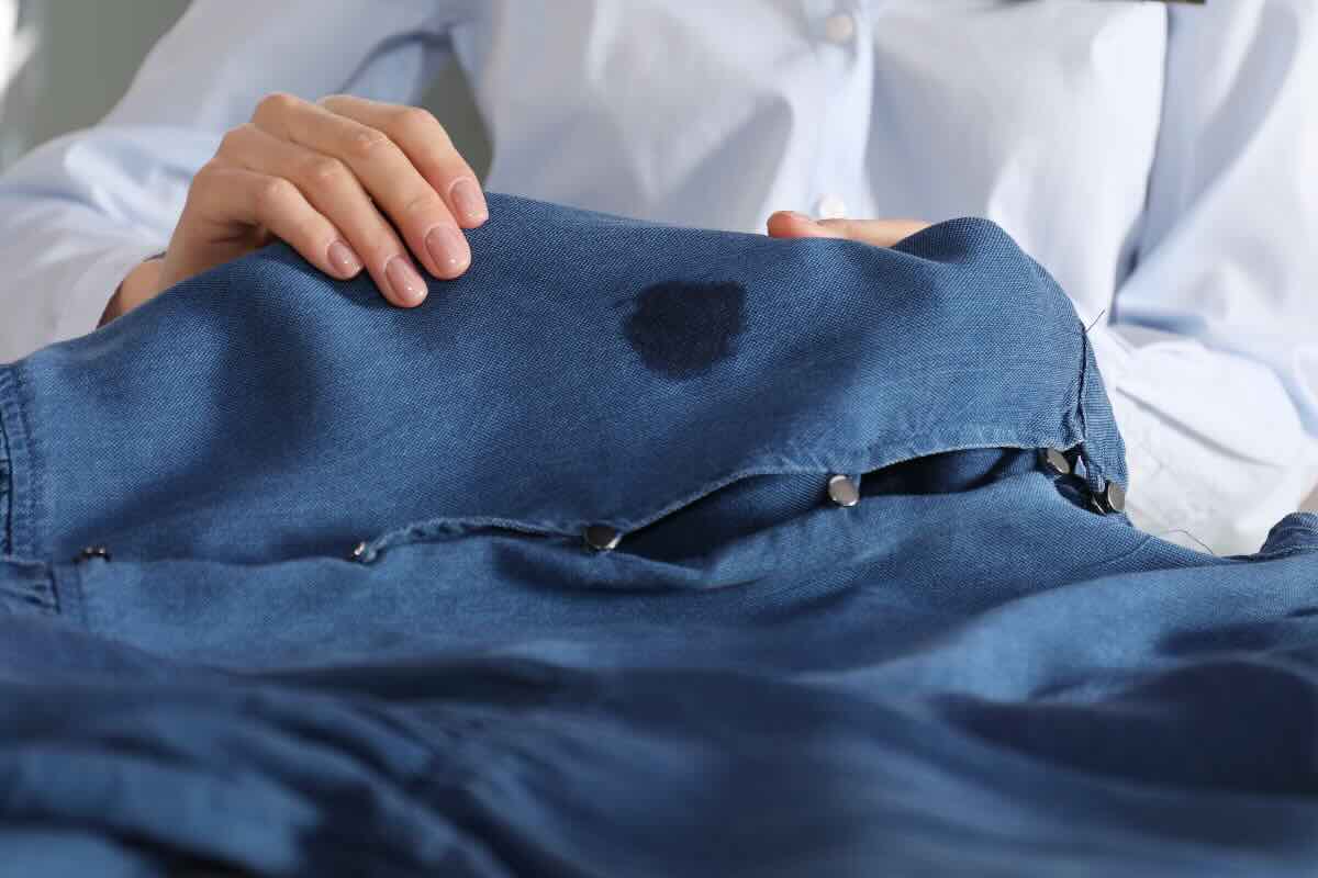 mani di donna che tengono indumento di jeans con macchia circolare