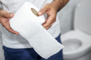 Uomo con rotolo carta igienica in mano, sullo sfondo c'è il WC