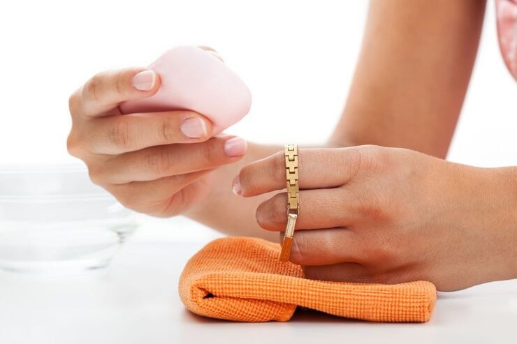 Mano di donna con in mano un bracciale d'oro, panno in microfibra arancione e saponetta rosa 