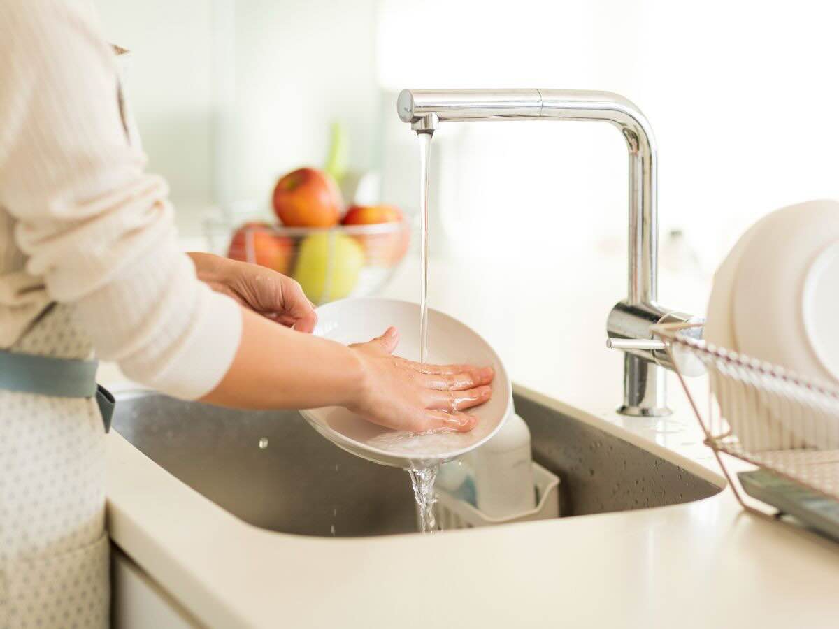 Mani di donna che lavano piatto sotto getto dell'acqua del lavandino