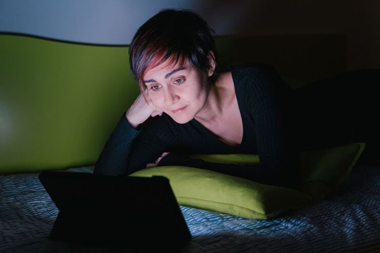 Donna con capelli corti e ciuffo rosso che guarda il PC sul letto al buio 